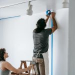 A man and woman working together on home renovation, applying painter's tape.