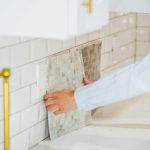 Person installing tile backsplash in a bright, modern kitchen setting.